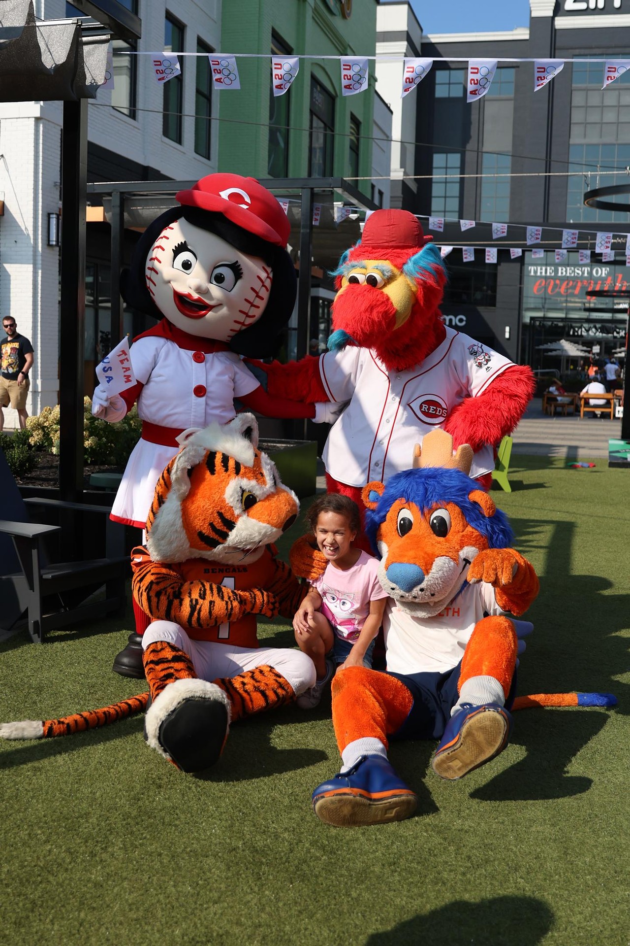 Cincinnati mascots take a photo with a participant at the Olympic Opening Ceremony celebration at Newport on the Levee on Friday, July 26, 2024.