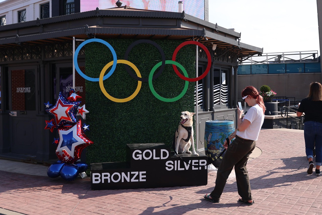 A woman takes a photo of her dog on the podium at the Olympic Opening Ceremony celebration at Newport on the Levee on Friday, July 26, 2024.